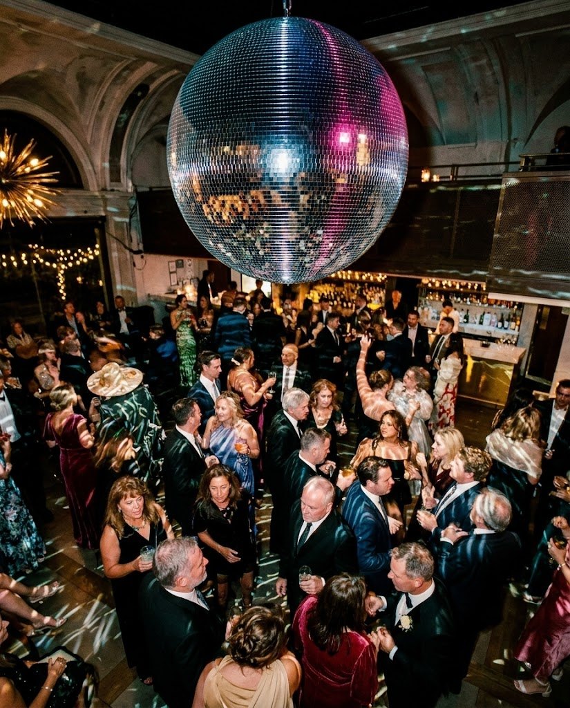 Guests dancing under a large disco ball at an evening reception